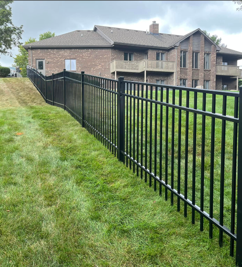 Black aluminum Bellamy fence running along a sloped lawn beside a brick building