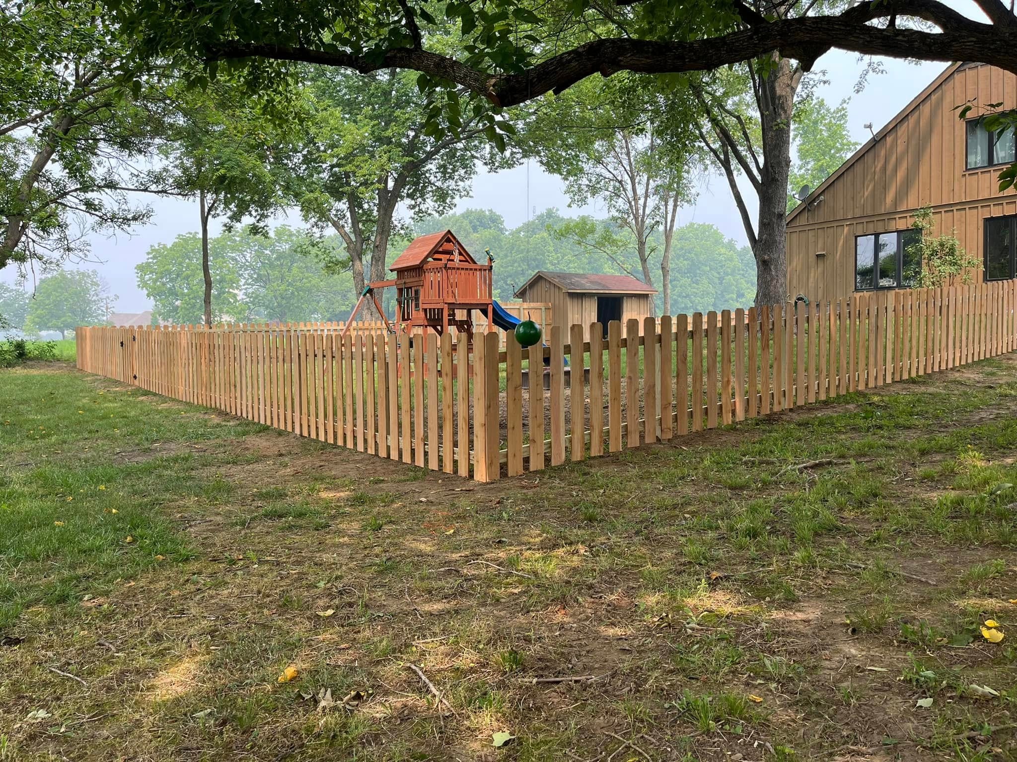 Wood spaced picket fence enclosing a backyard with a playset